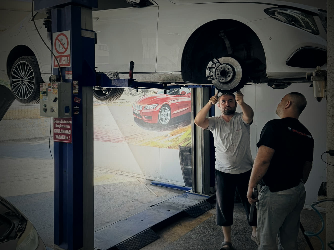 Merseda Oto ustaları lifte kaldırılmış Mercedes-Benz E Serisi'nin fren diski üzerinde çalışırken